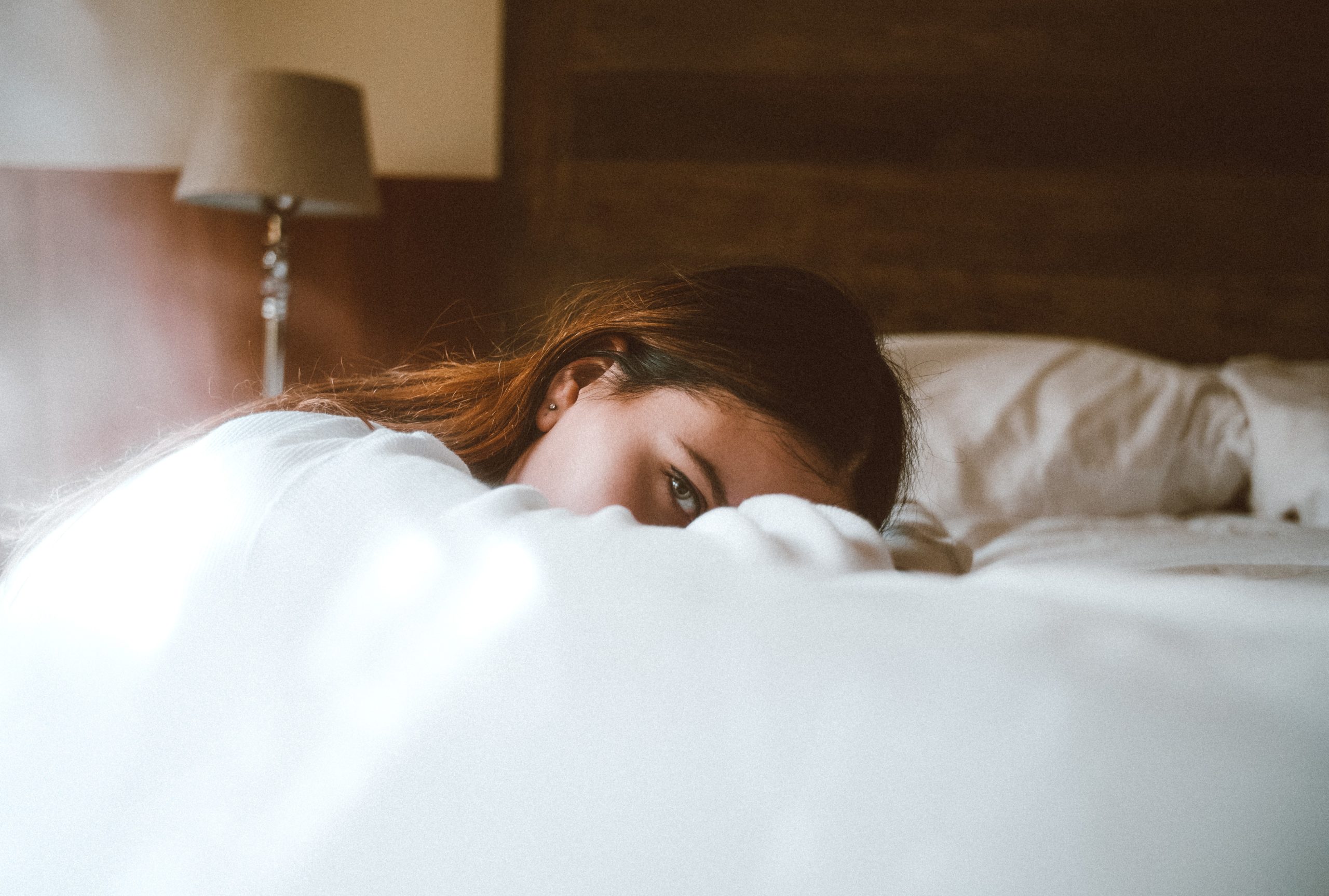 A woman with long brown hair slumped in bed with low energy.