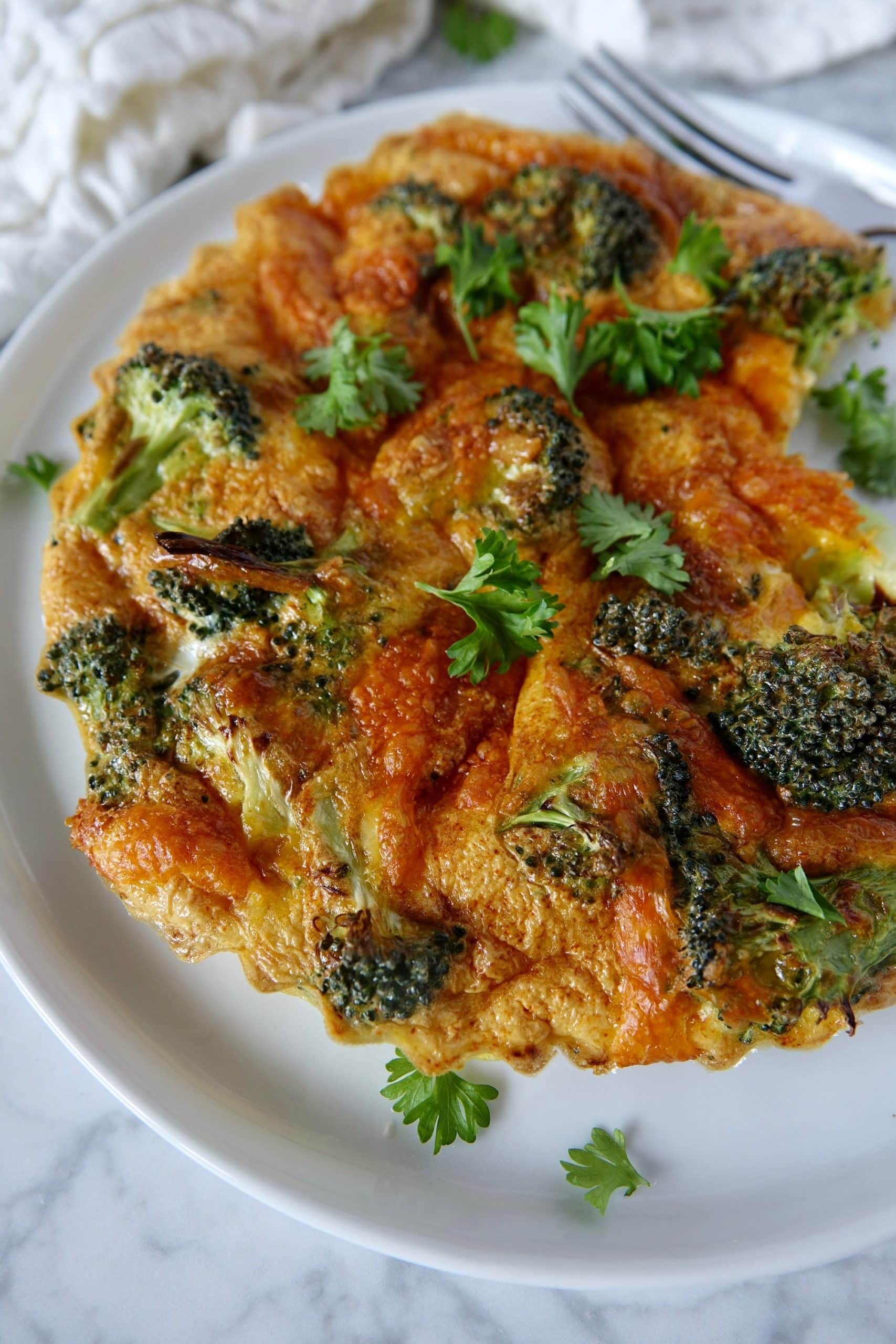 frittata with broccoli and cheddar cheese on a white plate on a light grey marble background