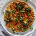 Frittata with broccoli and cheese on a white plate with a cream coloured kitchen towel and a couple of forks.
