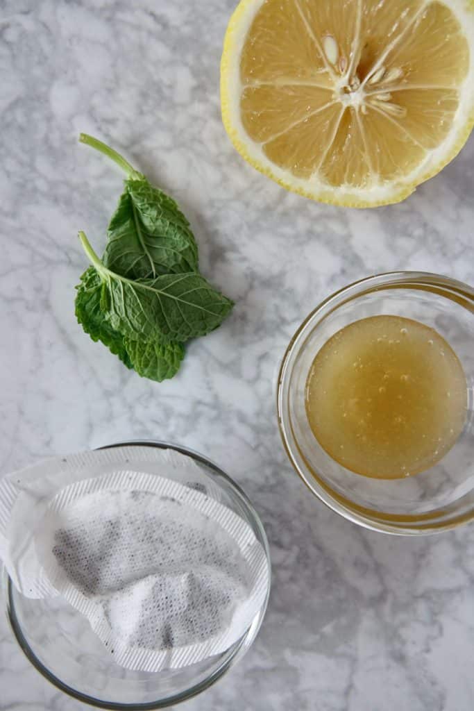 Ingredients laid out on a marble surface. Honey, tea bags, mint leaves, half a lemon.