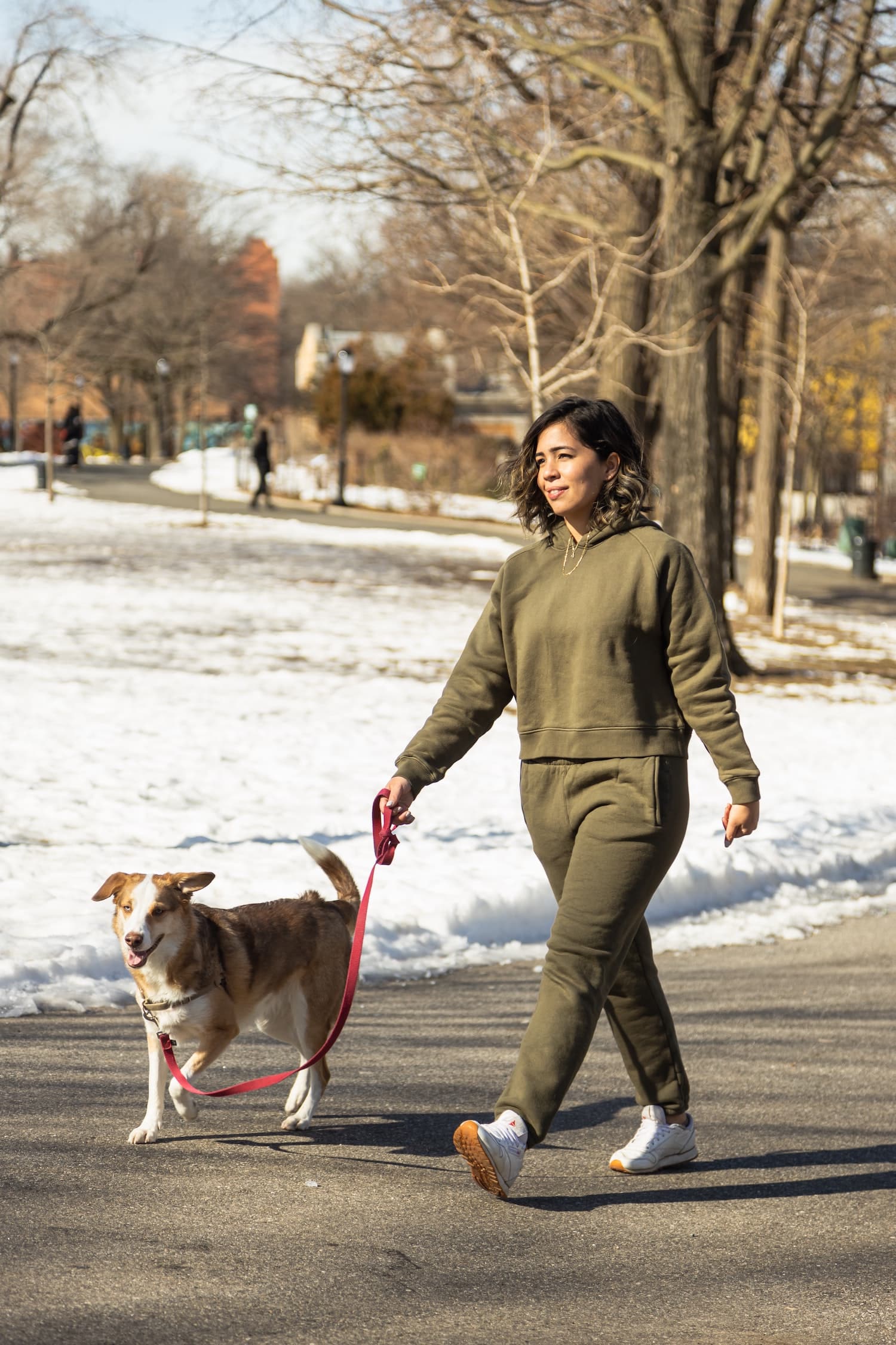 Women in green tracksuit walking her dog on a trail in the winter