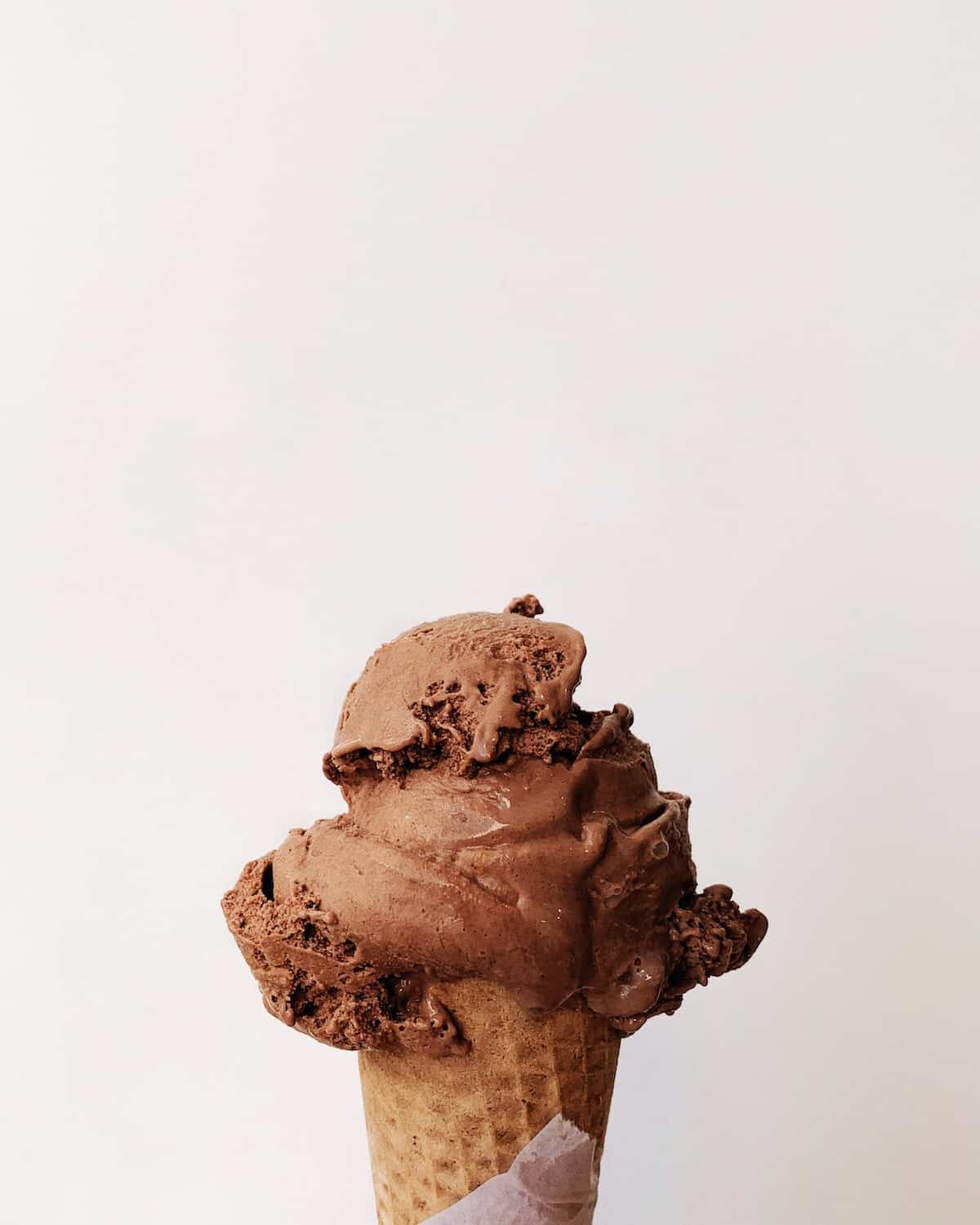 Photo of chocolate ice cream in cone held against a plane white wall