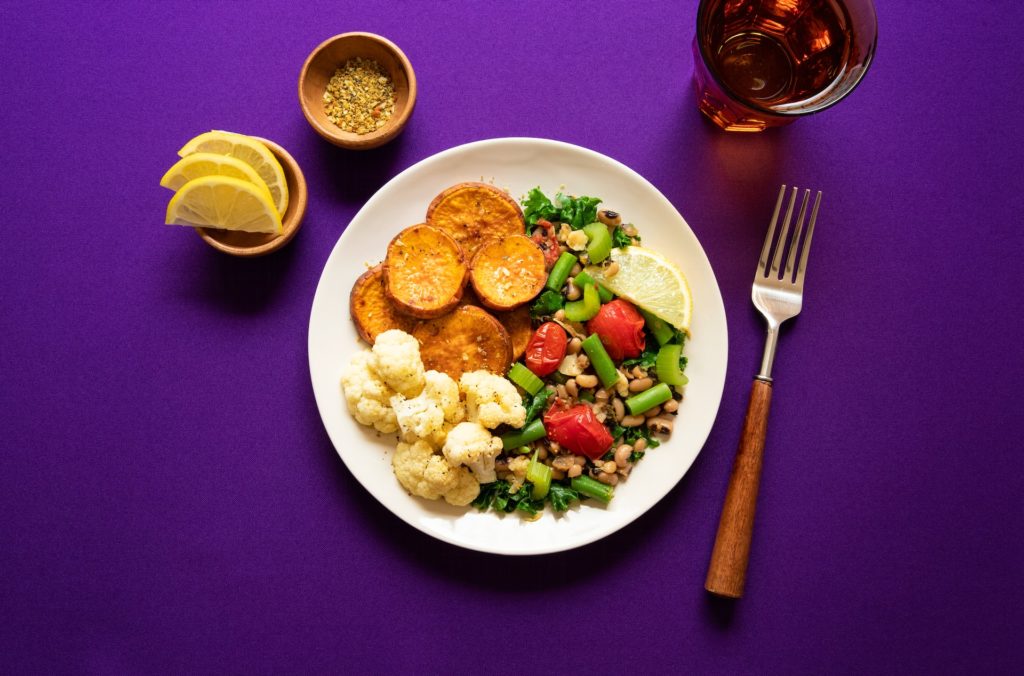 a balanced plate with sweet potatoes, cauliflower and black eyed peas on a purple countertop. 