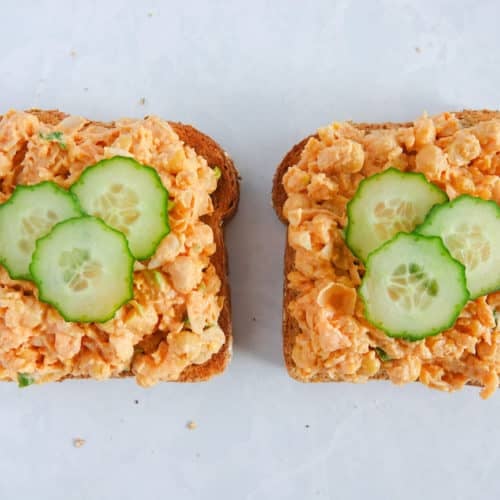 open faced chickpea salad sandwich with spicy chickpea mash and slices cucumbers, placed on white marble counter