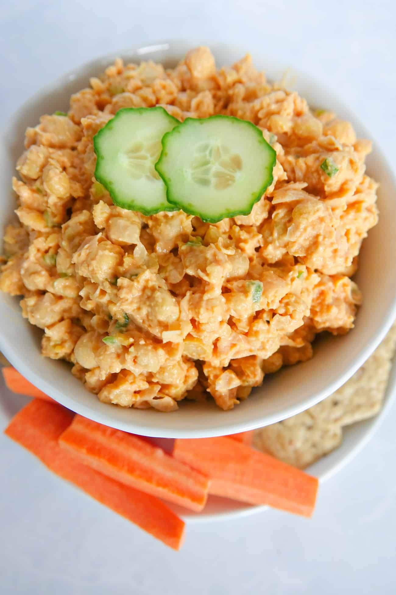 Spicy chickpea mash in a bowl, served with carrot sticks and seed crackers.
