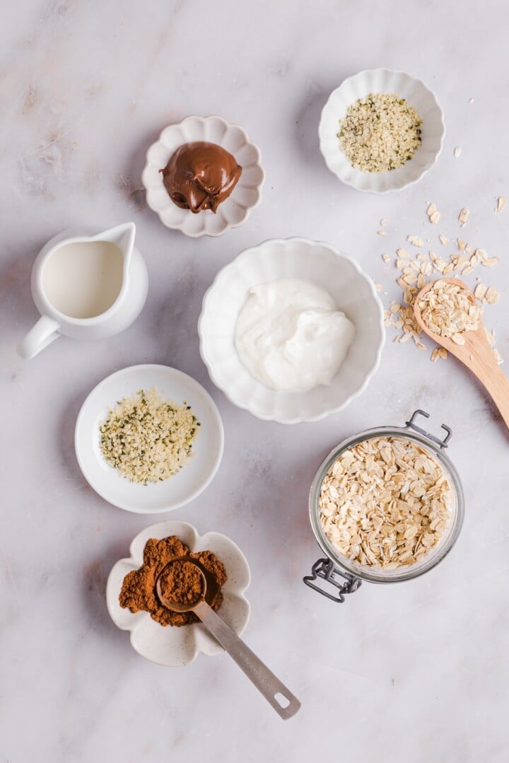 Ingredients for nutella overnights oats in small containers on a marble counter.