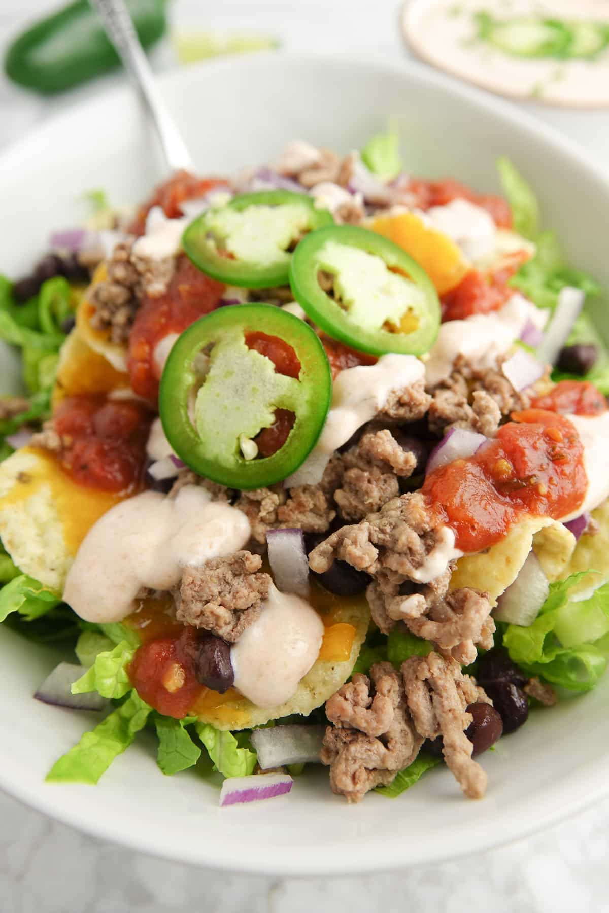 Taco salad in a white bowl placed on a white marble countertop.