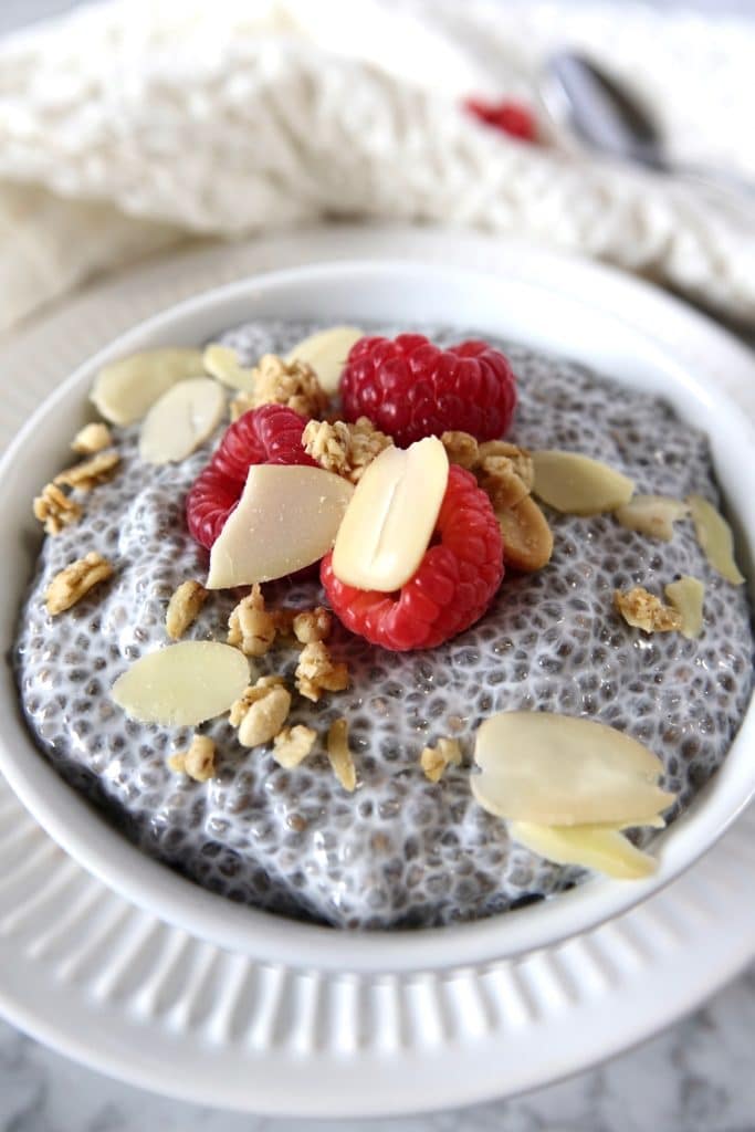 Chia pudding in white bowl on marble counter top, topped with raspberries and almond slices
