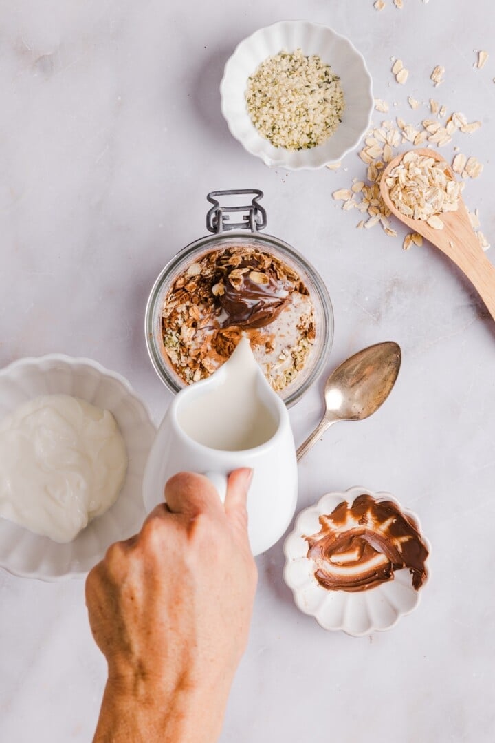 Ingredients for nutella overnight oats stirred in a glass jar.