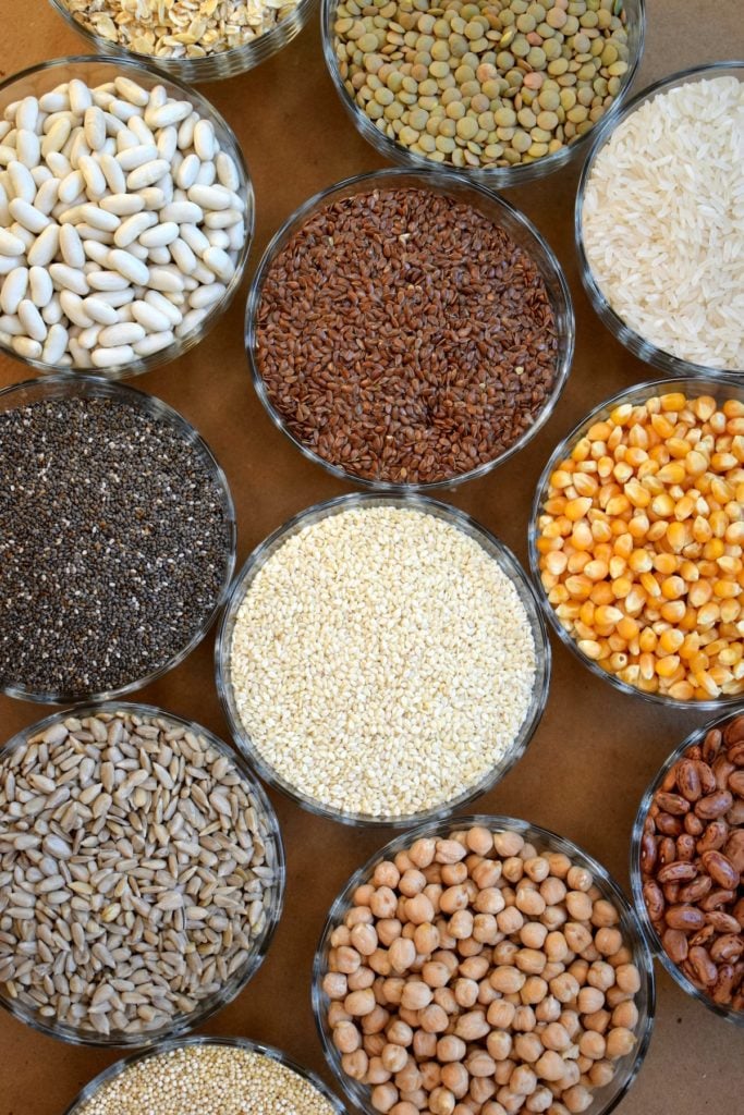 Bowls of dried whole grains displayed on wooden table.