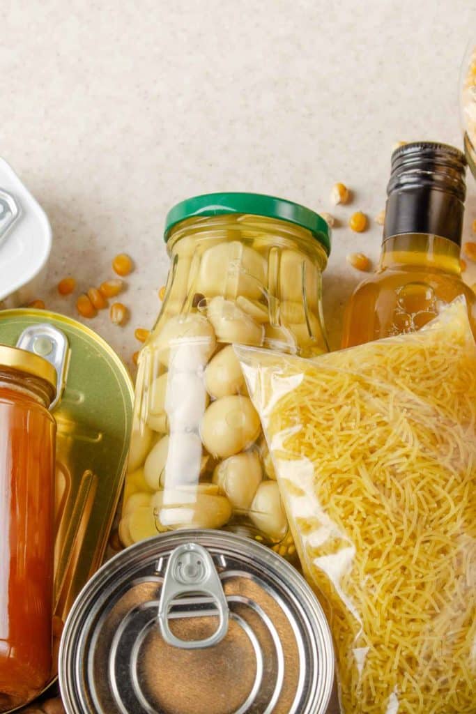 Close up photo of non-perishable foods on a light colored counter, including jarred beans, oil and canned food.