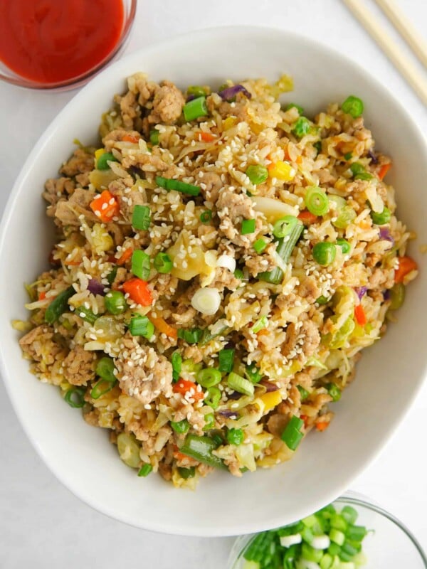 Unstuffed egg rolls in a bowl displayed in white bowl on white marble counter. Displayed with sriracha, green onions and chopsticks. Sprinkled with sesame seeds.
