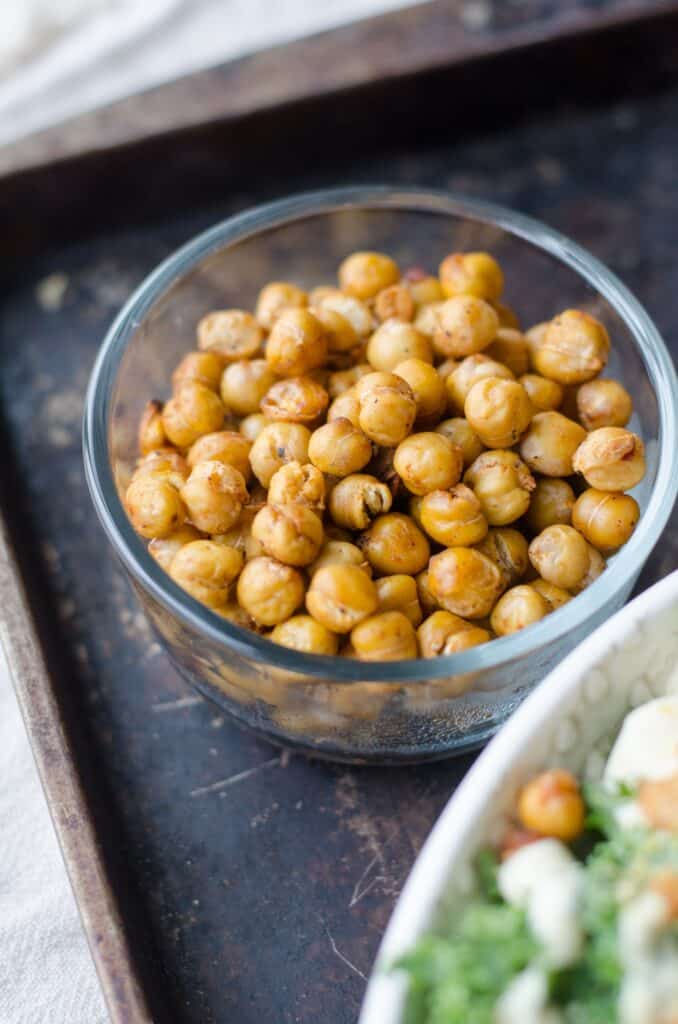 Roasted chickpeas in glass bowl on baking tray.