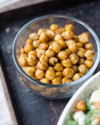 Roasted chickpeas in glass bowl on baking tray.