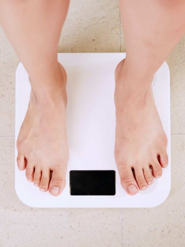 Woman stepping on a weighing scale on a tile floor. No number is appearing on the scale.