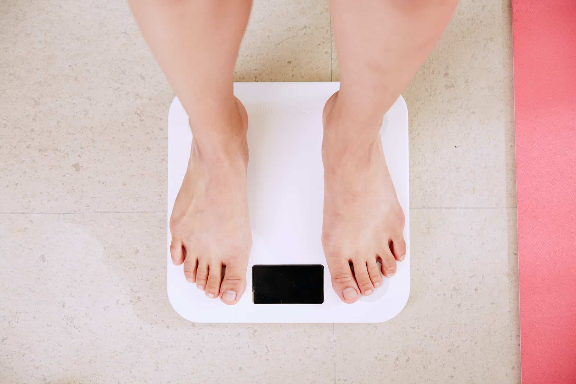 Woman stepping on a weighing scale on a tile floor. No number is appearing on the scale.