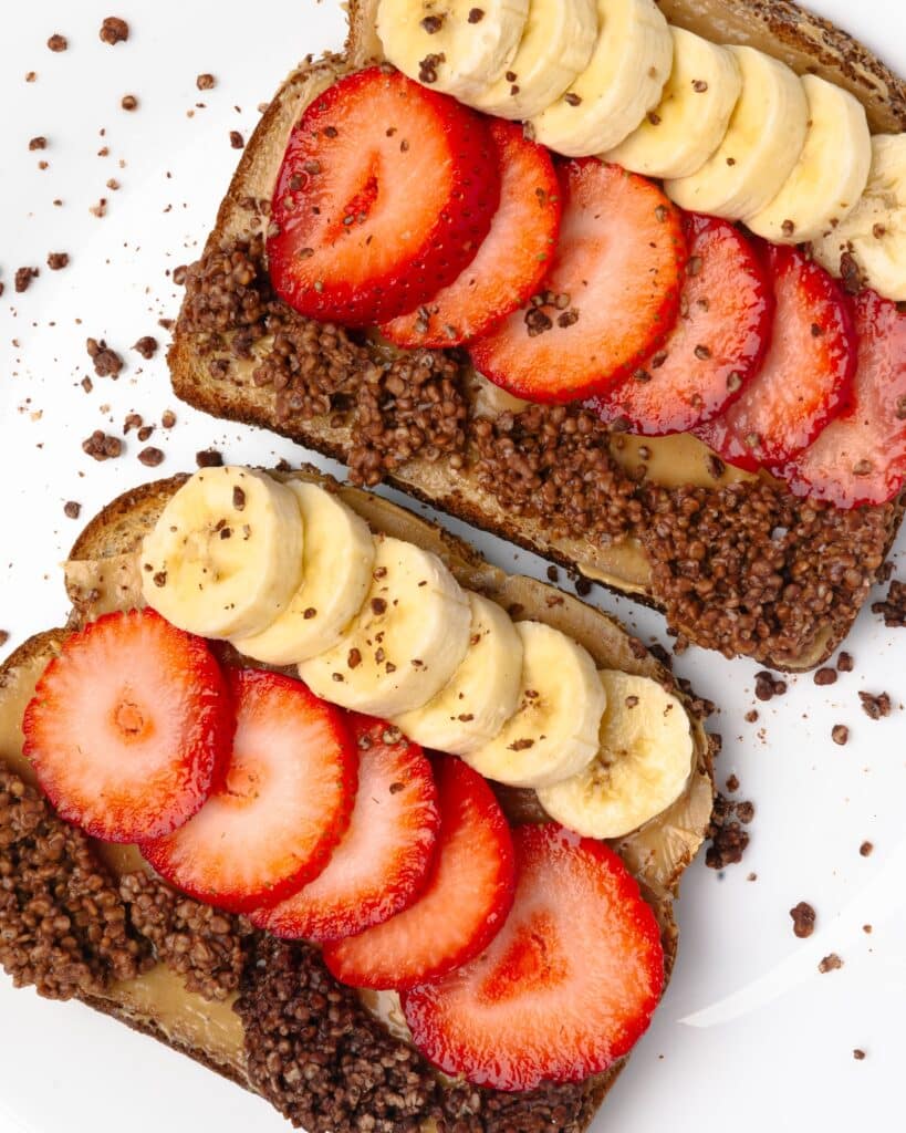 Two slices of peanut butter toast on a white plate topped with slices strawberries and banana. 