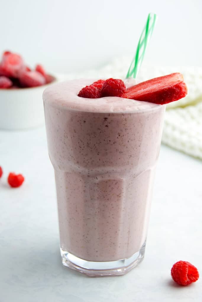 Pink smoothie with strawberries and raspberries in a glass with a green striped straw, displayed on a white marble counter.