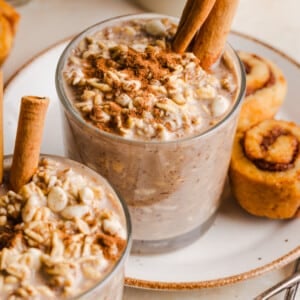 Cinnamon roll overnight oats in glass cup, garnished with cinnamon sticks.