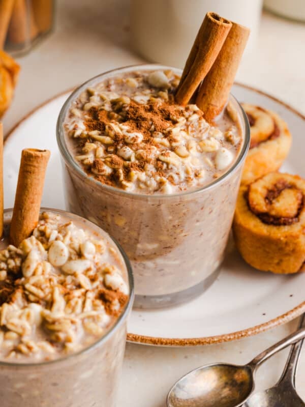 Cinnamon roll overnight oats in glass cup, garnished with cinnamon sticks.