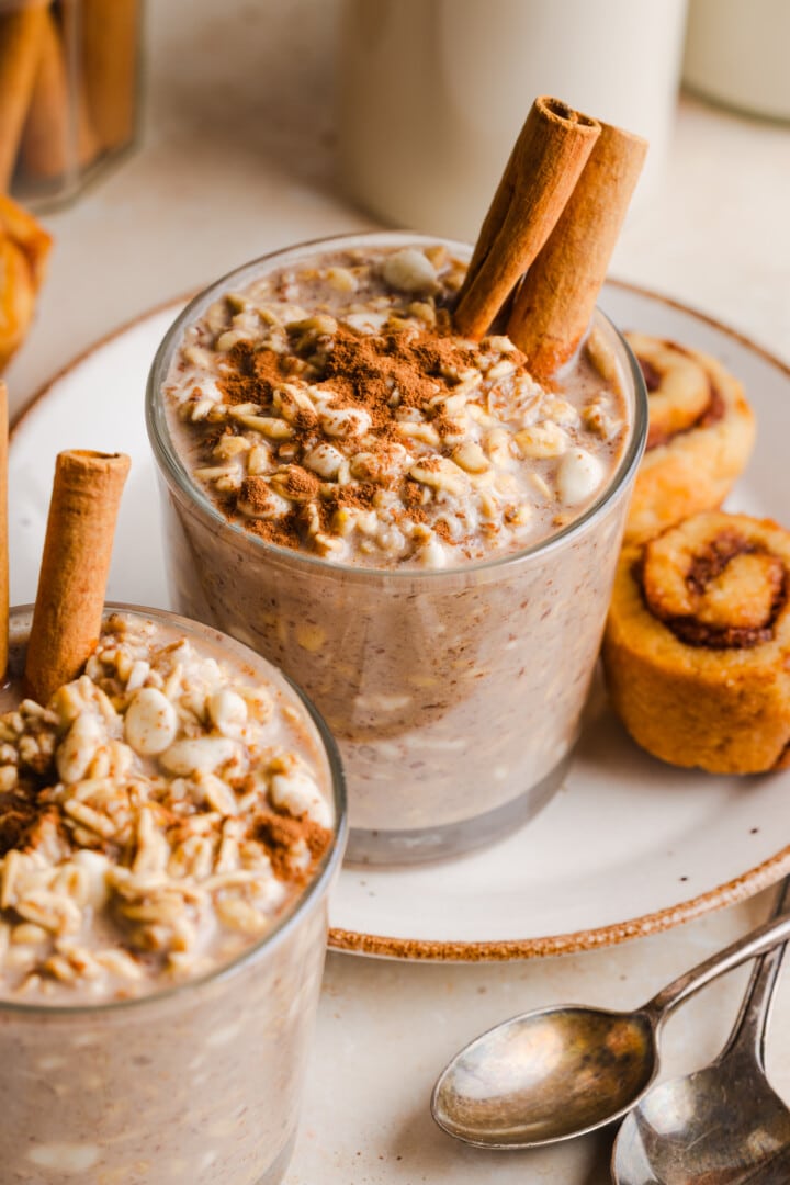 Cinnamon roll overnight oats in glass cup, garnished with cinnamon sticks.