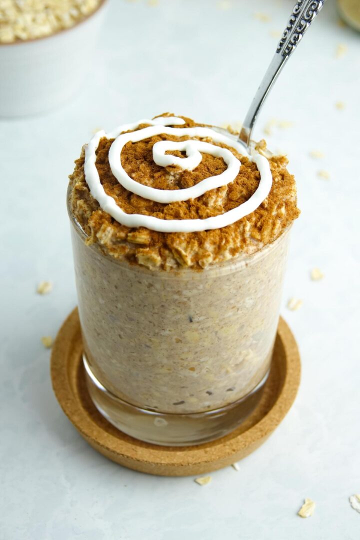 Photo of cinnamon roll overnight oats presented in a clear glass with cinnamon and a swirl of yogurt on top.