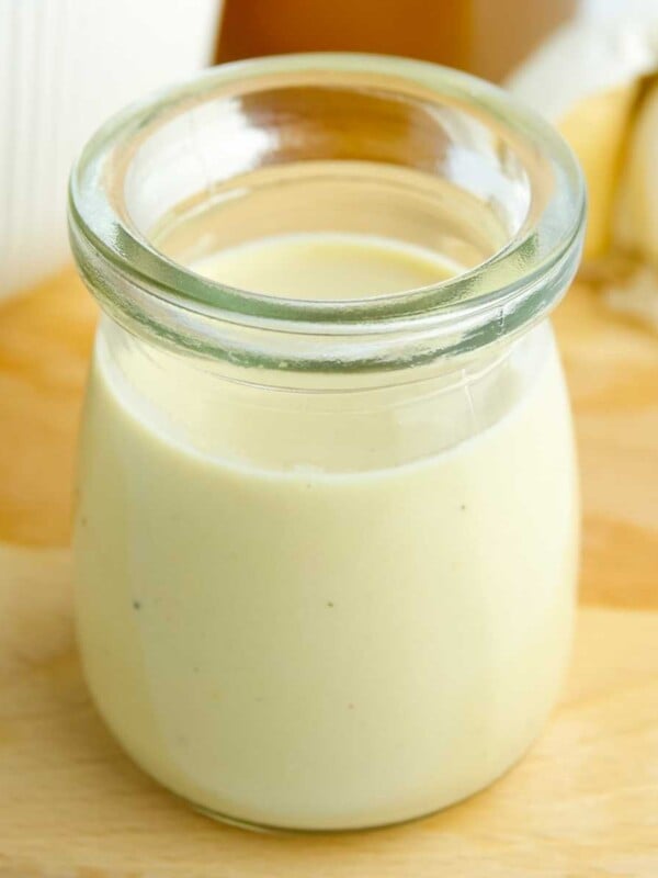 Hummus salad dressing in an open, small glass jar on top of a wooden cutting board.