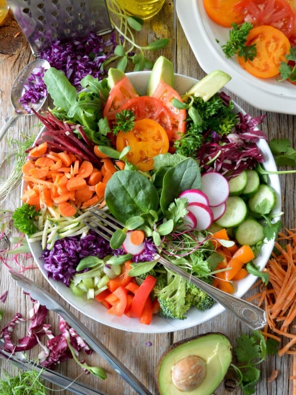 Birdseye photo of a colorful salad with lots of different vegetables, displayed next to ingredients and olive oil.