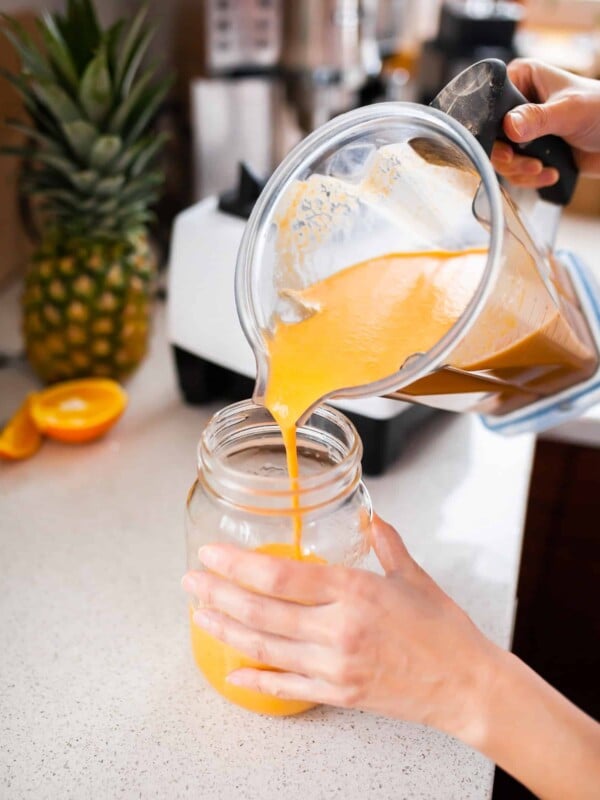 Woman pouring an orange-colored smoothie from a blender into a glass.