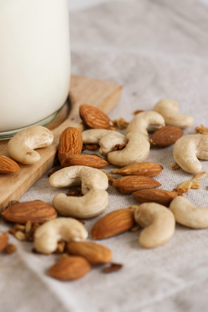 Raw cashews and almonds sprinkled on a tea towel with nut milk in the background.