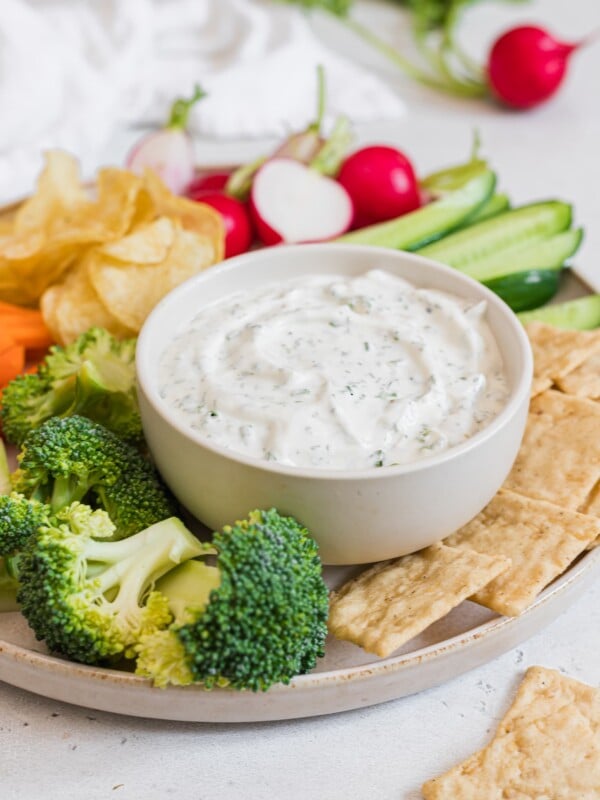 Bowl of healthy ranch dip with greek yogurt displayed in a small white bowl, served with assorted raw vegetables, crackers, and chips.