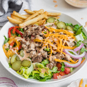 Cheeseburger bowl with ground beef and frozen french fries assembled and un-mixed in a white bowl.