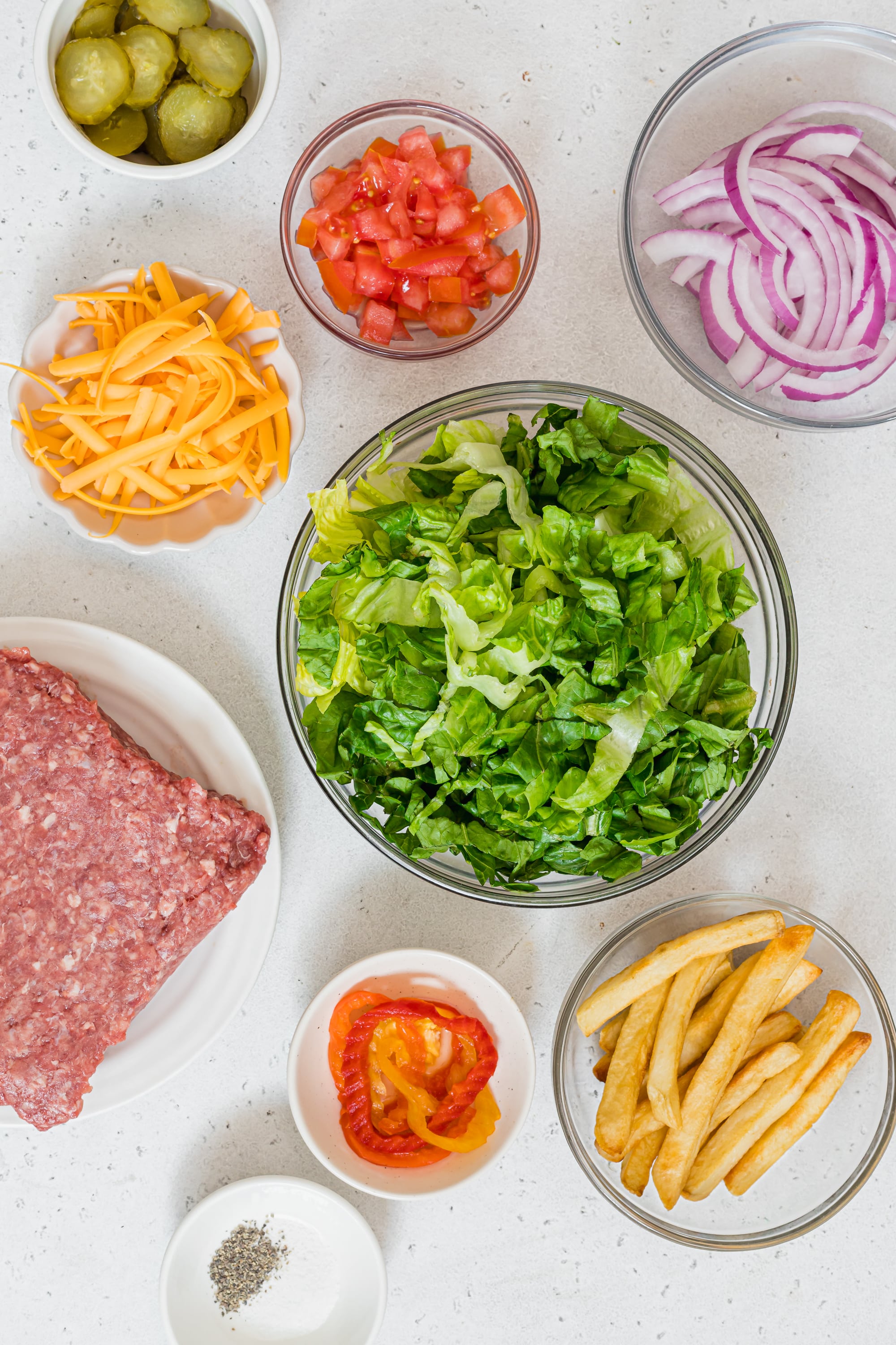 Ingredients for cheeseburger bowls displayed in bowls on a whiter countertop.