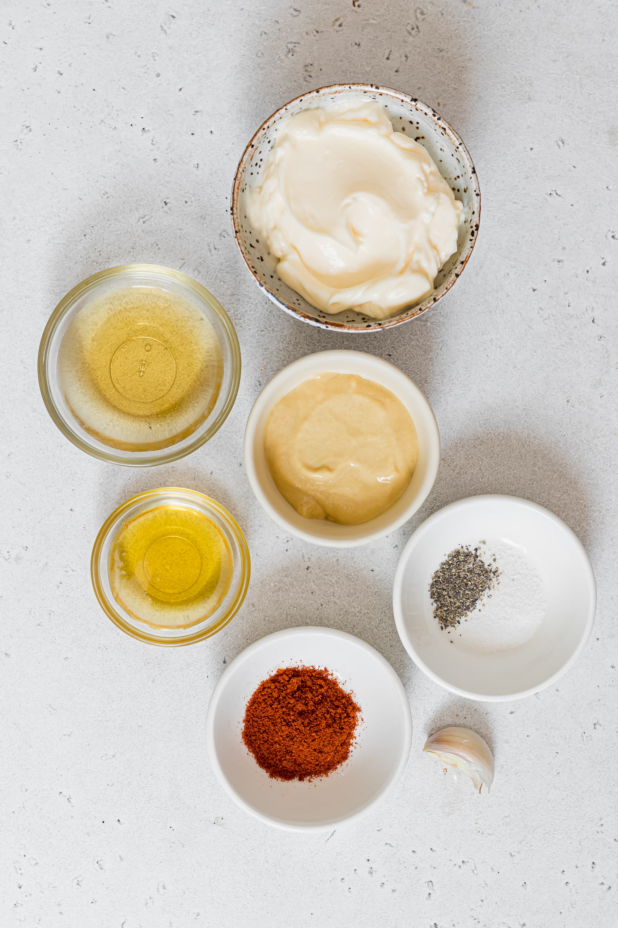 Ingredients for mustard vinaigrette displayed in small bowls on a white countertop.