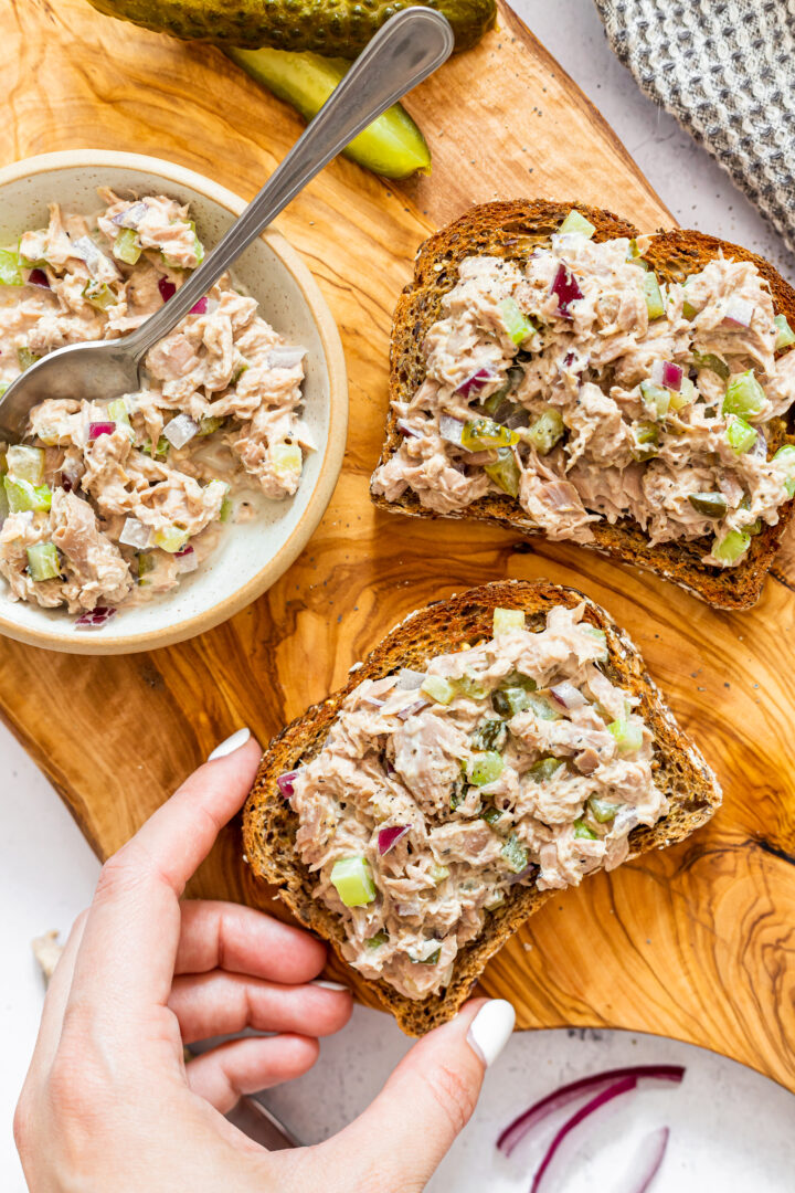 Birdseye view of open-faced tuna salad sandwiches on whole grain bread, displayed on a wood cutting board.