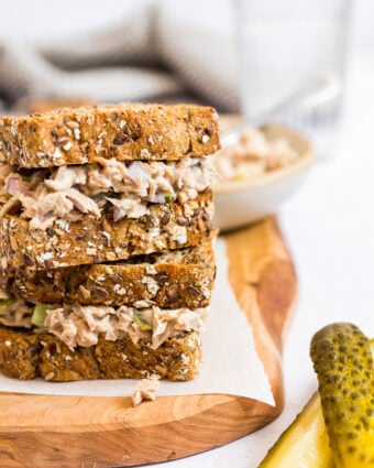 Tuna salad sandwich with dill pickled on a wooden cutting board.