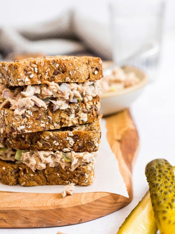 Tuna salad sandwich with dill pickled on a wooden cutting board.