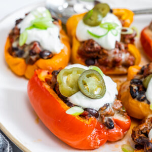 Photo of taco stuffed bell peppers on a white plate, topped with sour cream and pickled jalapeno peppers.