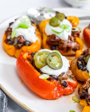 Photo of taco stuffed bell peppers on a white plate, topped with sour cream and pickled jalapeno peppers.