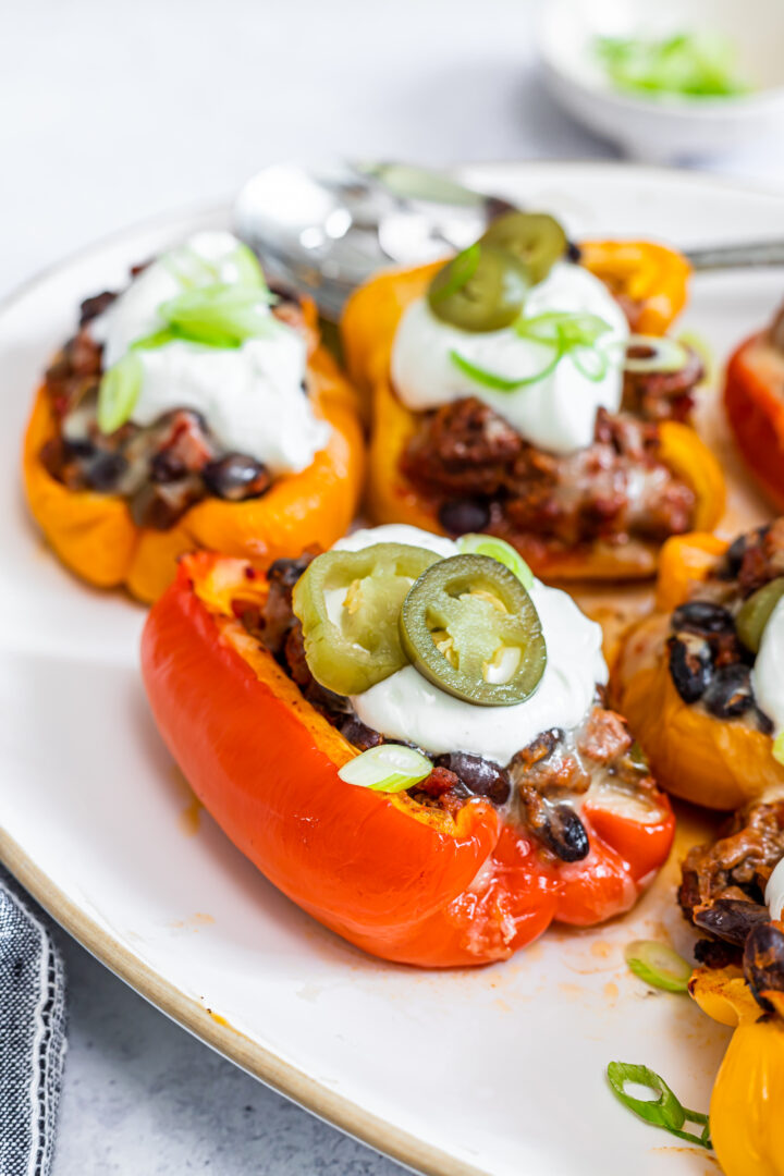 Photo of taco stuffed bell peppers on a white plate, topped with sour cream and pickled jalapeno peppers.
