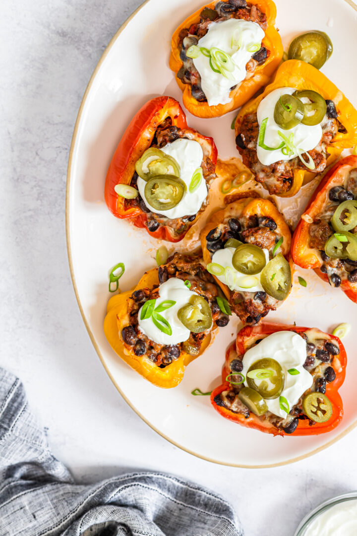 Stuffed peppers with toppings on a serving dish on a white marble counter.