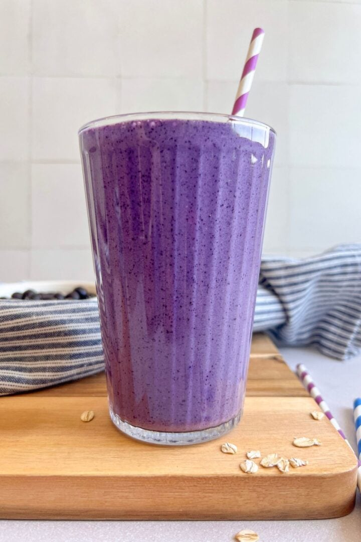 Thick, refreshing, and packed with 35 grams of protein, this blueberry smoothie makes the easiest healthy breakfast to take on the go. Blueberry protein smoothie in a glass with a straw on a cutting board.