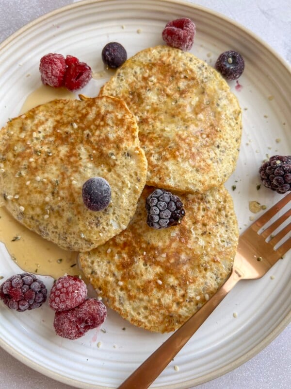 3 ingredient banana oat pancakes topped with maple syrup and frozen berries