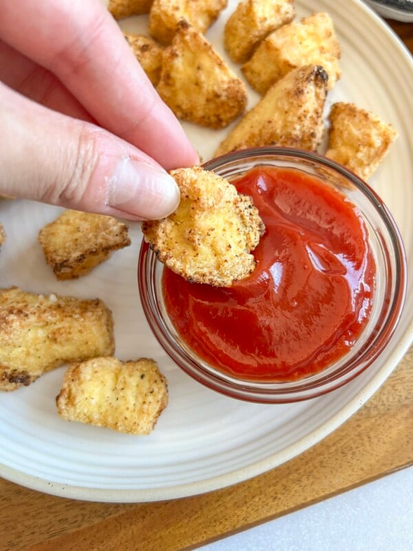 Air fryer tofu nuggets on a plate, being dipped into a small bowl of ketchup