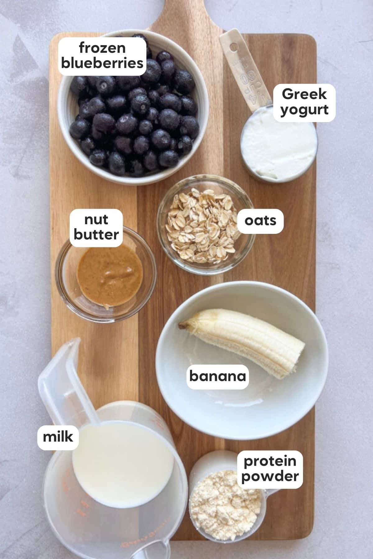 Labeled photo of ingredients in blueberry protein shake displayed on a wooden board on a marble counter