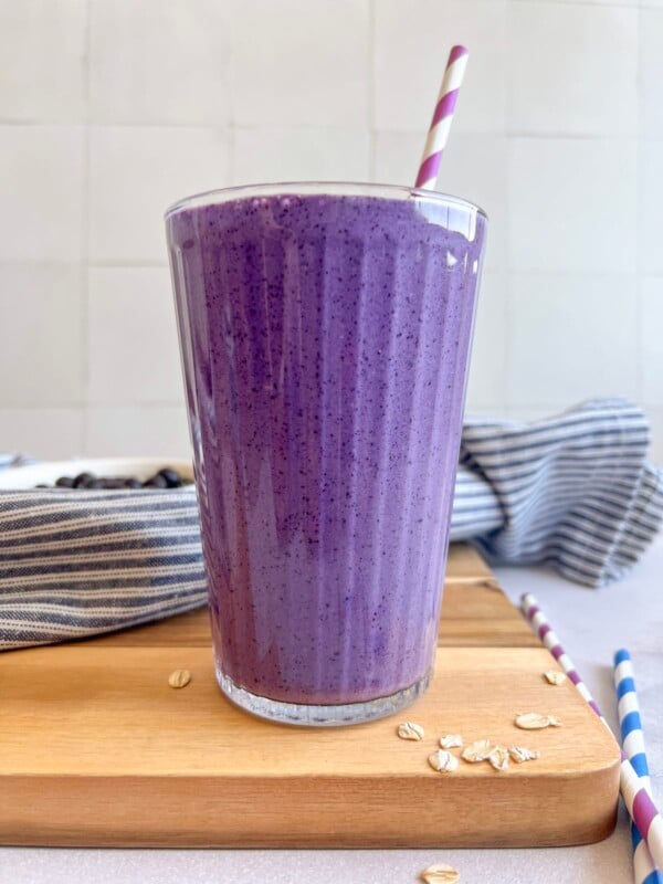 Blueberry muffin smoothie in a glass with a purple striped straw