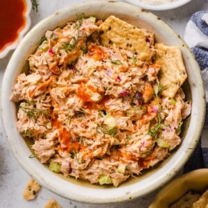 Buffalo tuna salad dip in a white bowl with seedy crackers.