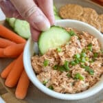 Hand dipping a cucumber slice into a small dish of buffalo tuna dip