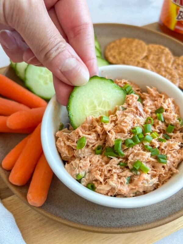 Hand dipping a cucumber slice into a small dish of buffalo tuna dip
