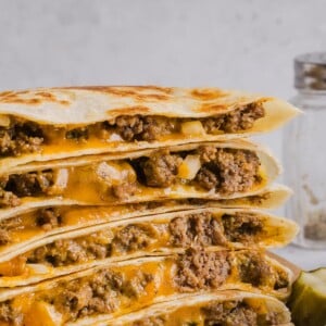 Cheeseburger quesadillas sliced and stacked on a wood cutting board.